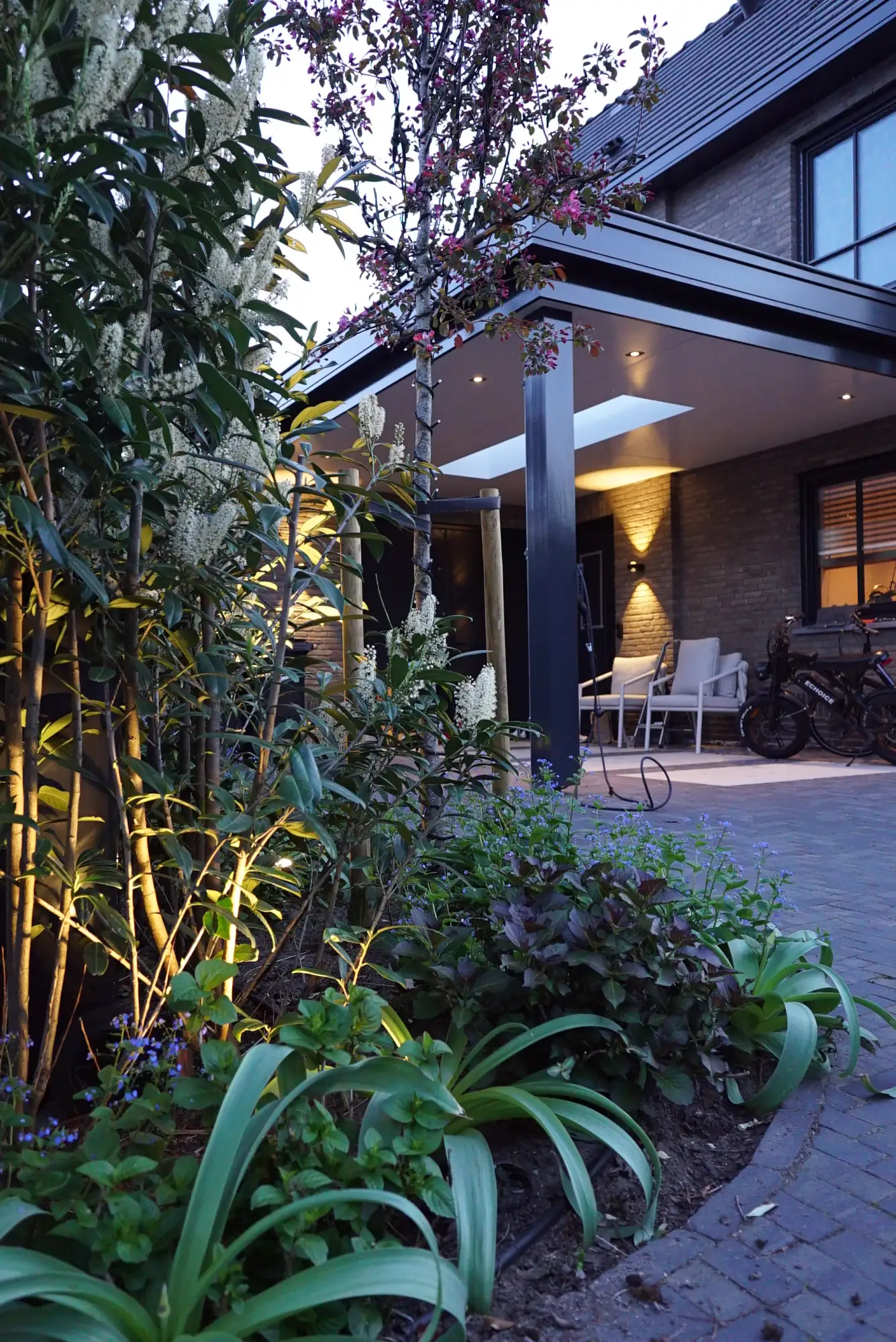 Tuin met uplights in de borders en een verlichte veranda in de avond