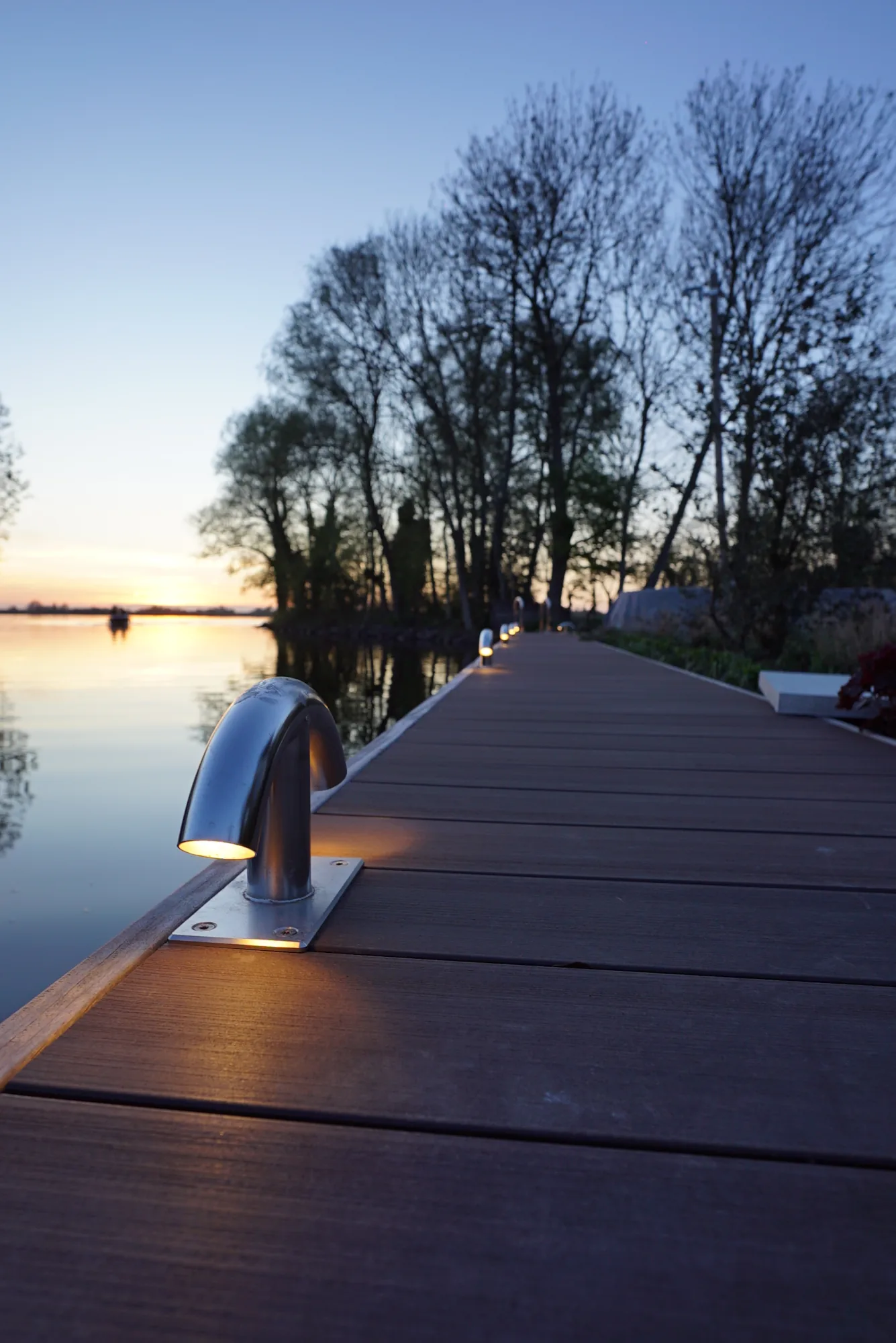 Vlonder aan het water met verzonken dekverlichting bij zonsondergang