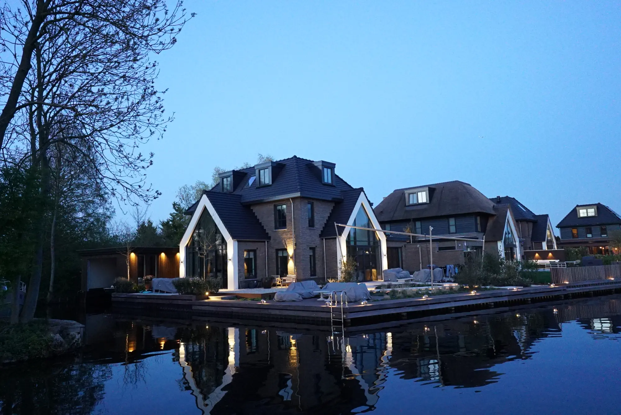 Villa aan het water met gevel- en terrasverlichting in het blauwe uur