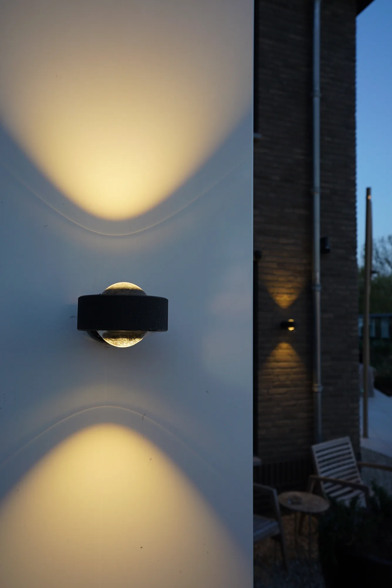 Wandlamp met licht naar boven en beneden tegen een witte gevel